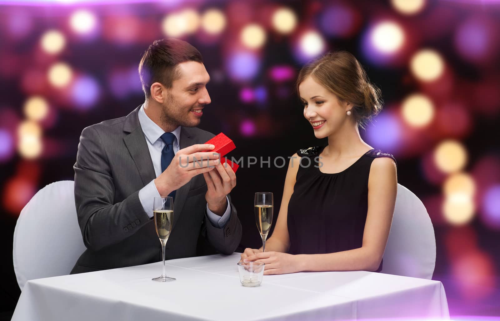 restaurant, couple and holiday concept - excited young woman looking at boyfriend with gift box at restaurant