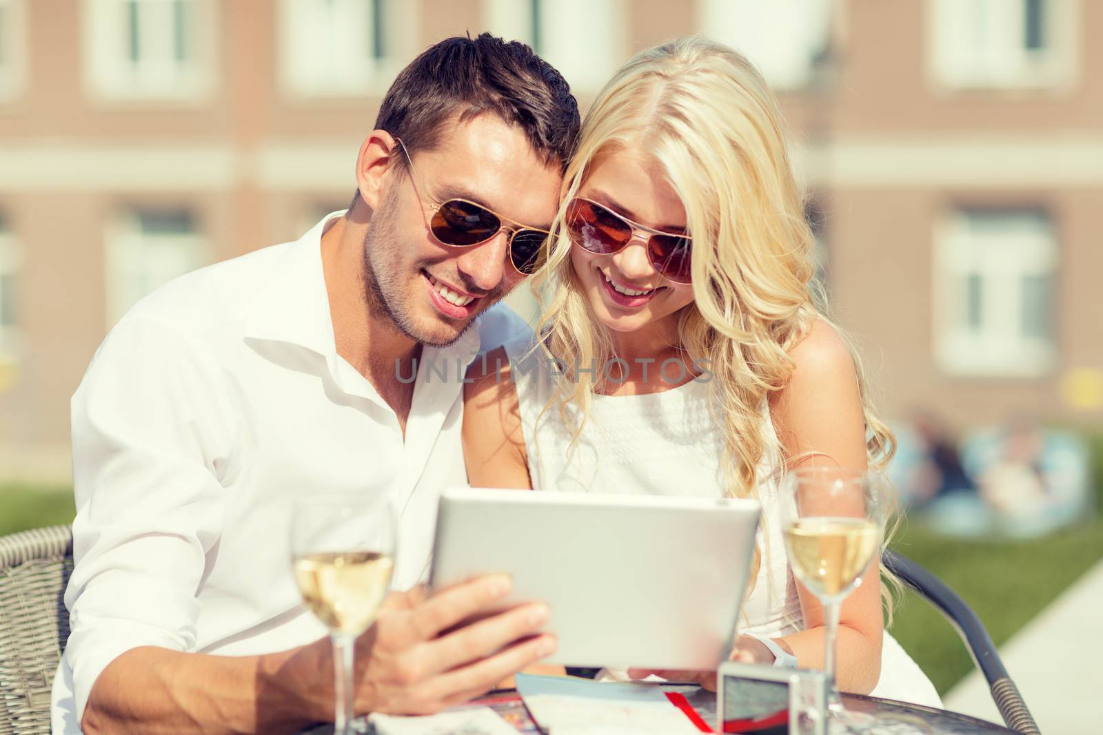 summer holidays, dating and technology concept - couple looking at tablet pc in cafe in the city