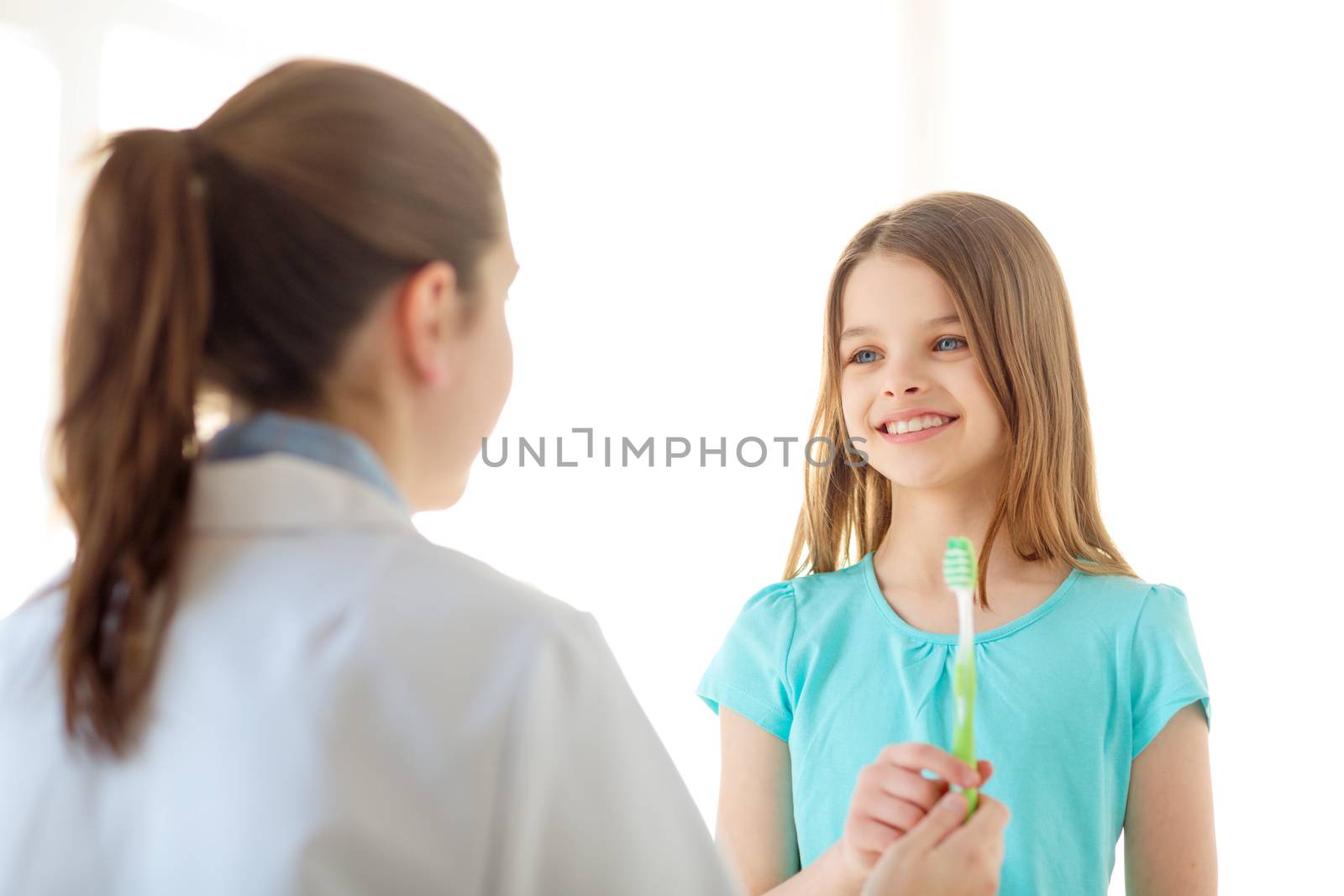 female doctor giving toothbrush to smiling girl by dolgachov