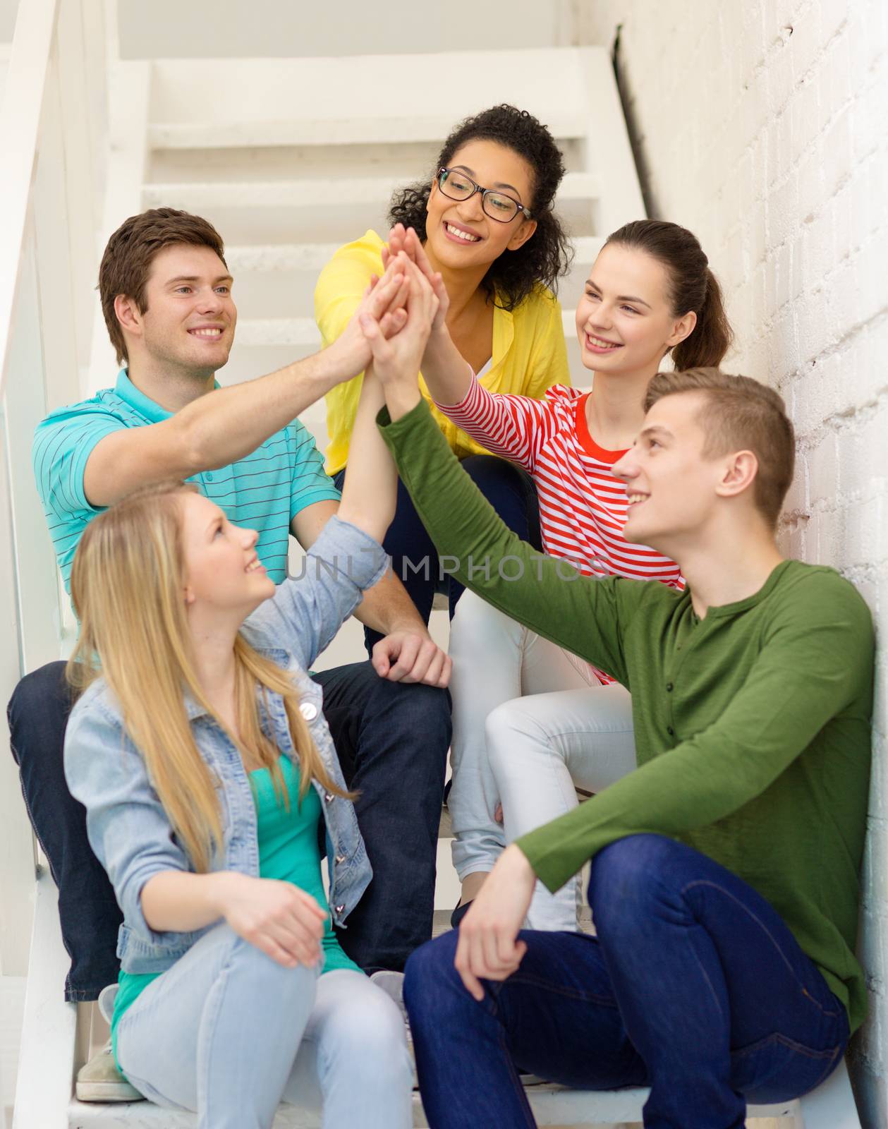 education and happiness concept - smiling students making high five gesture sitting on staircase