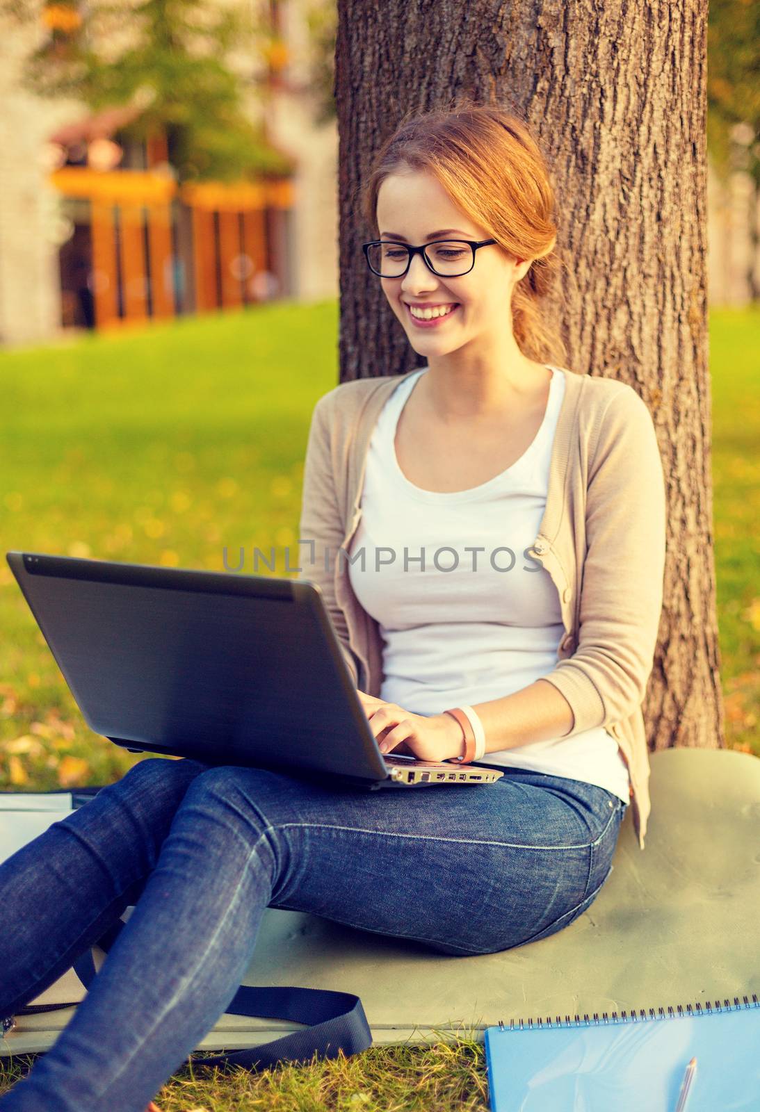 education, technology and internet concept - smiling teenager in eyeglasses with laptop computer and notebook