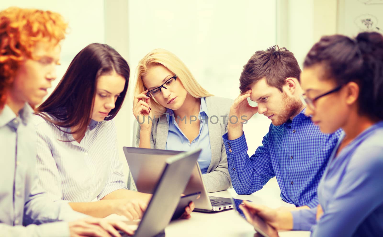 business, office and startup concept - depressed creative team with table pc and laptop computers working in office