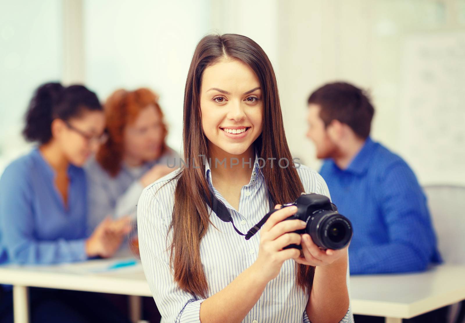 business, office and startup concept - smiling female photographer with photocamera in office with team on the back
