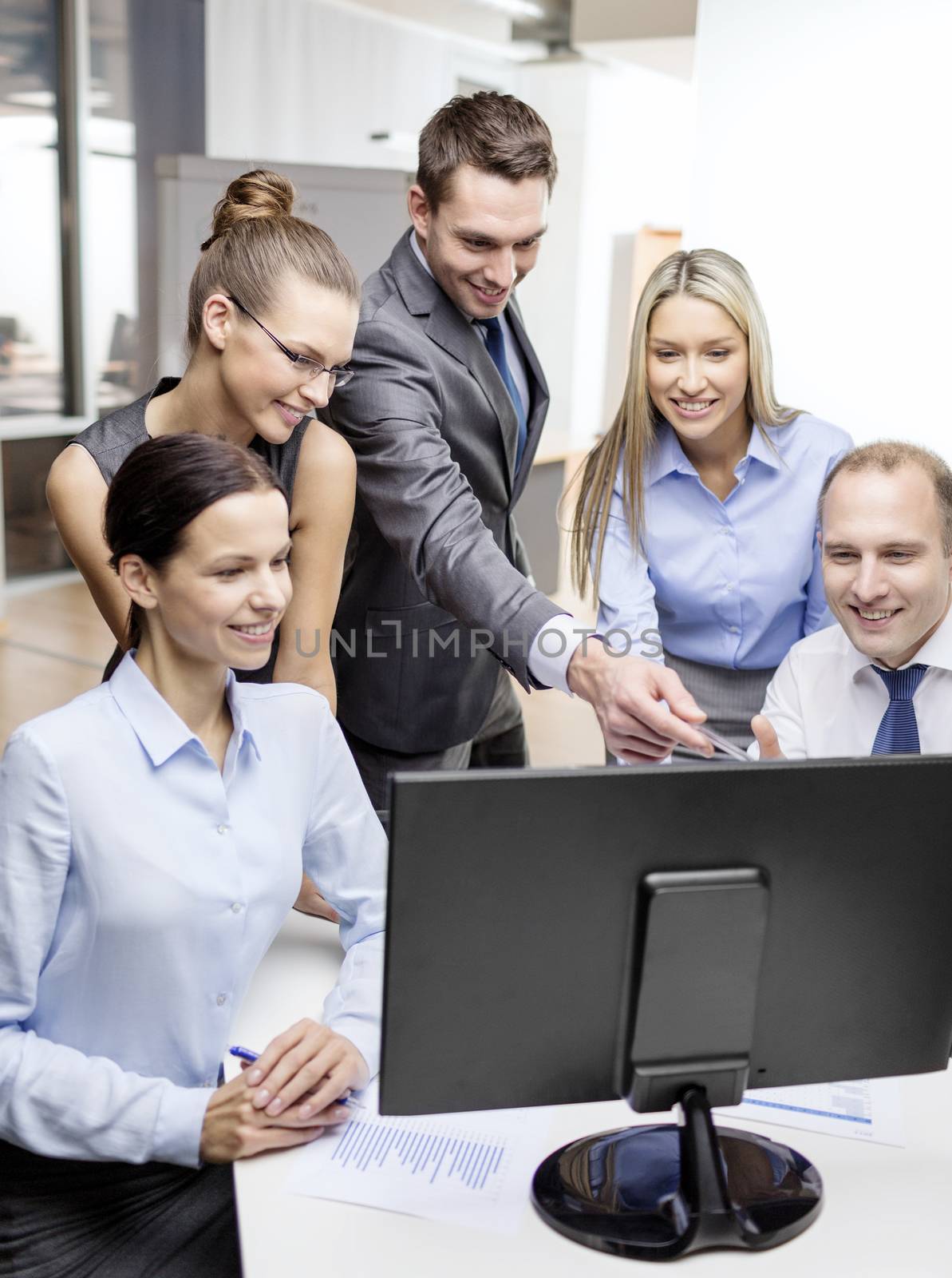 business, technology and office concept - smiling business team with computer monitor having discussion in office