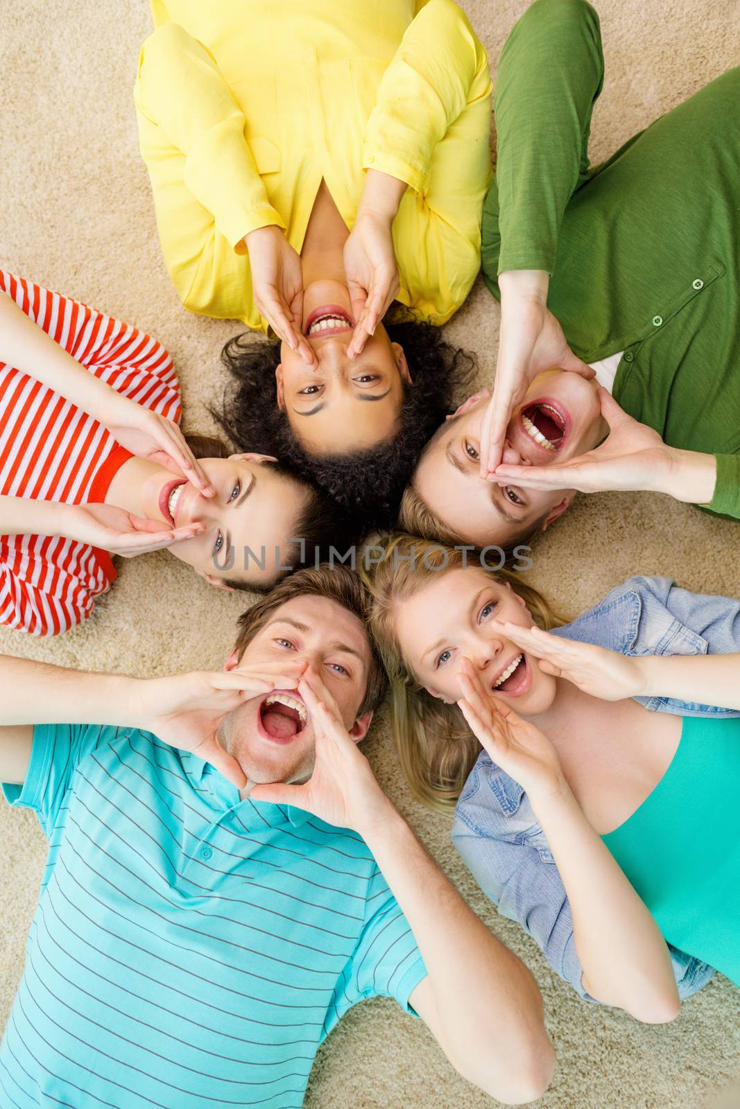 education and happiness concept - group of young smiling people lying down on floor in circle screaming and shouting