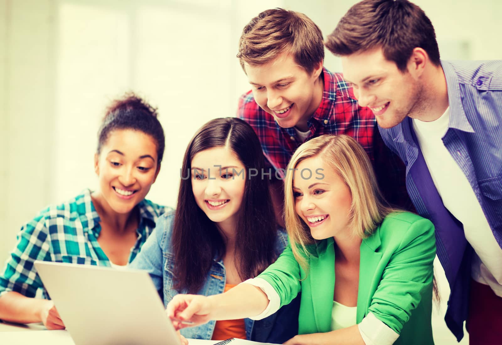 smiling students looking at laptop at school by dolgachov