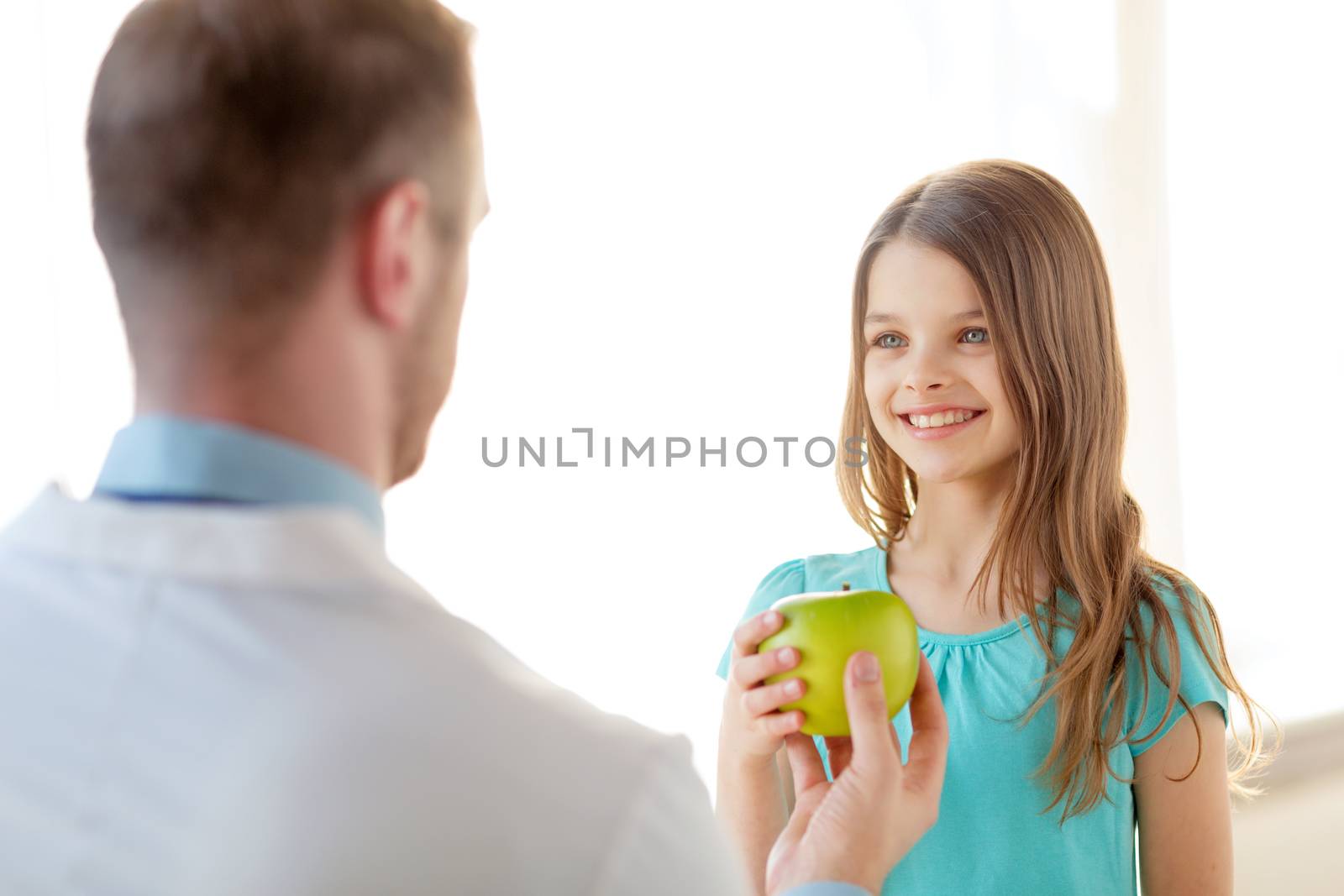 healthcare, child and medicine concept - male doctor giving an apple to smiling little girl