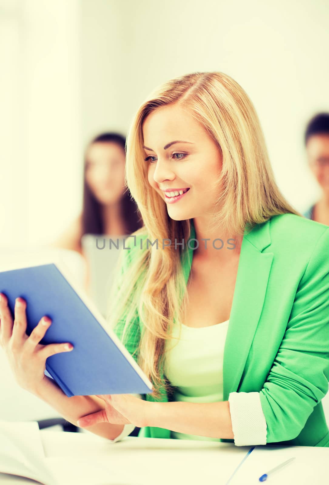 smiling young girl reading book at school by dolgachov