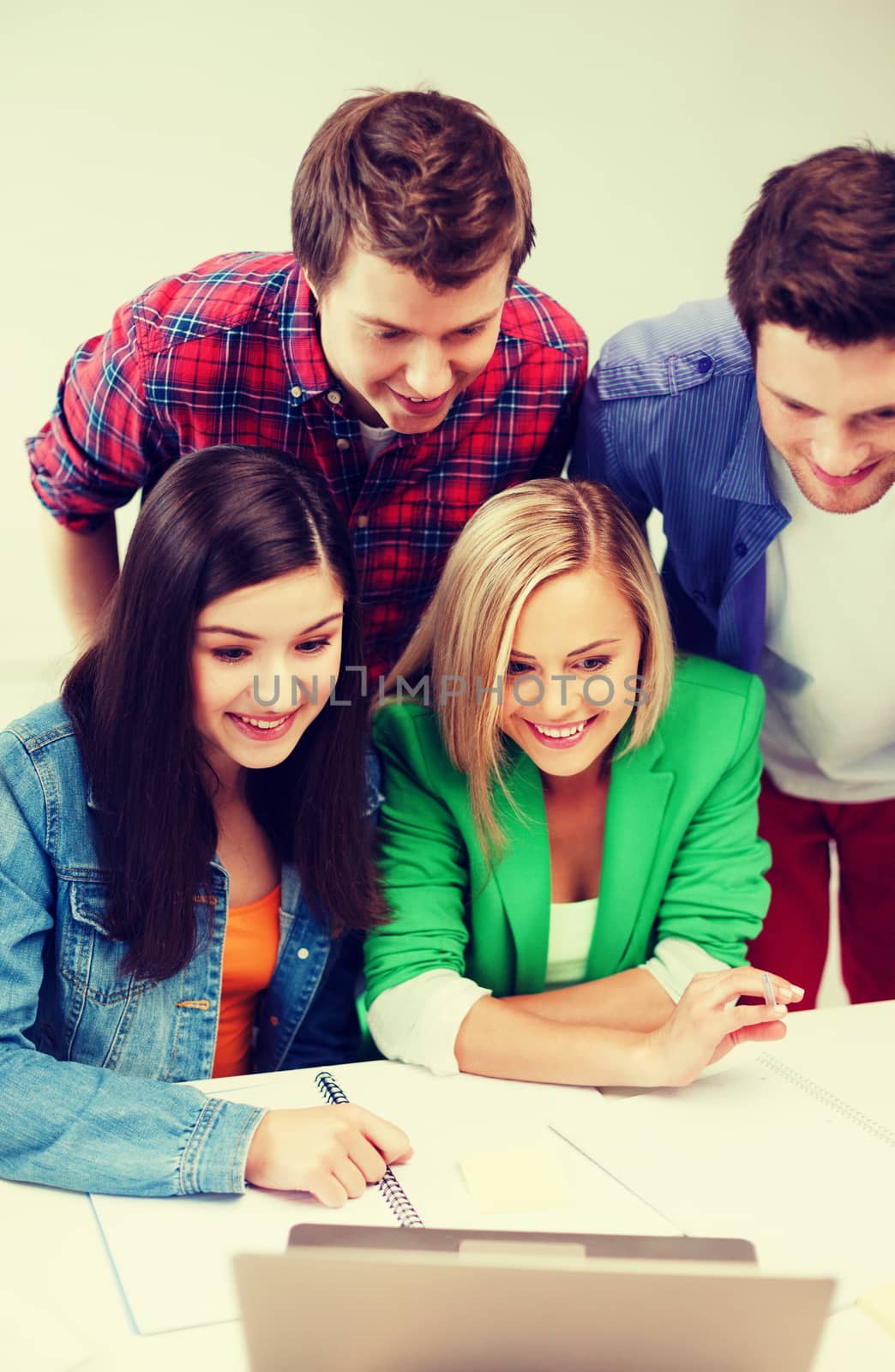 smiling students looking at laptop at school by dolgachov