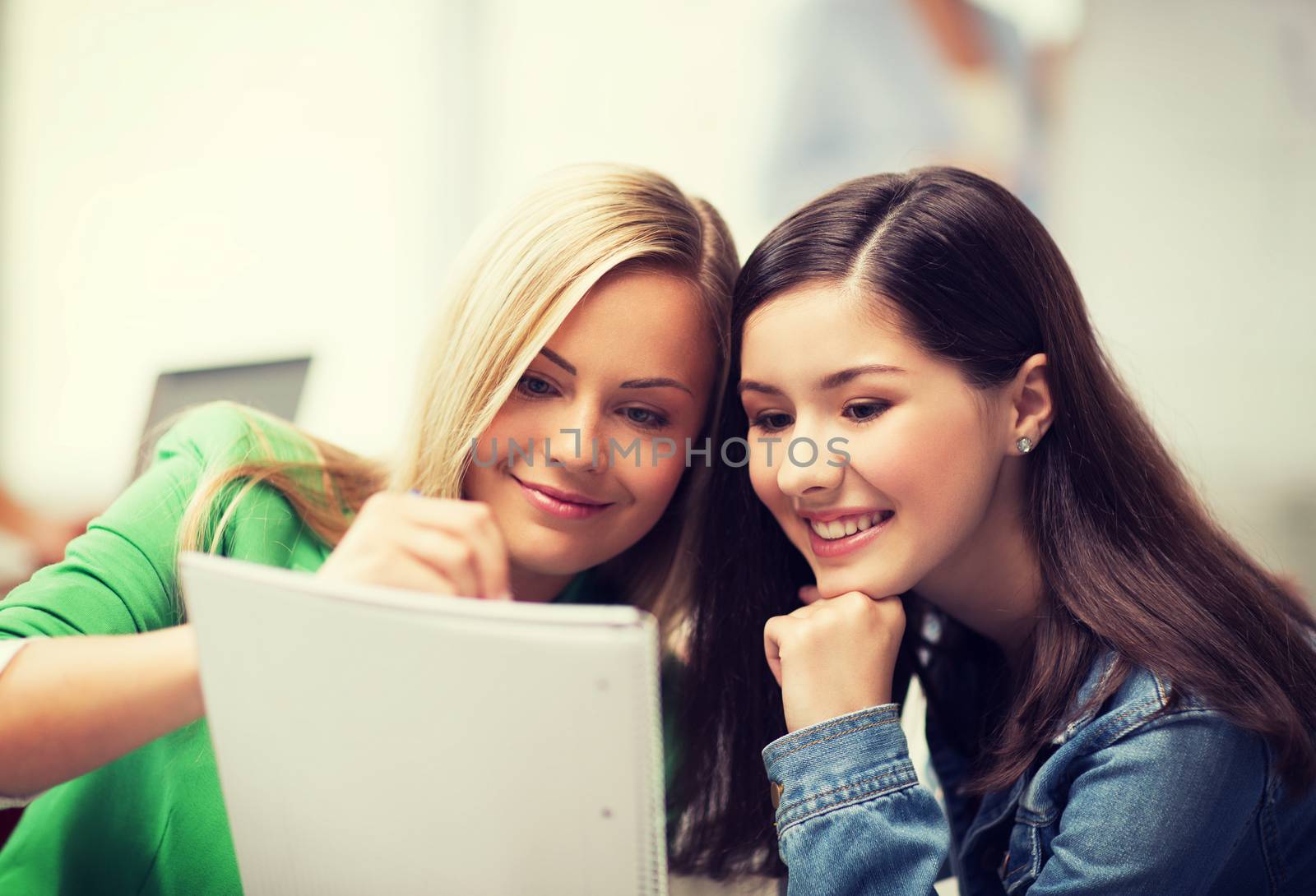 student girls pointing at notebook at school by dolgachov