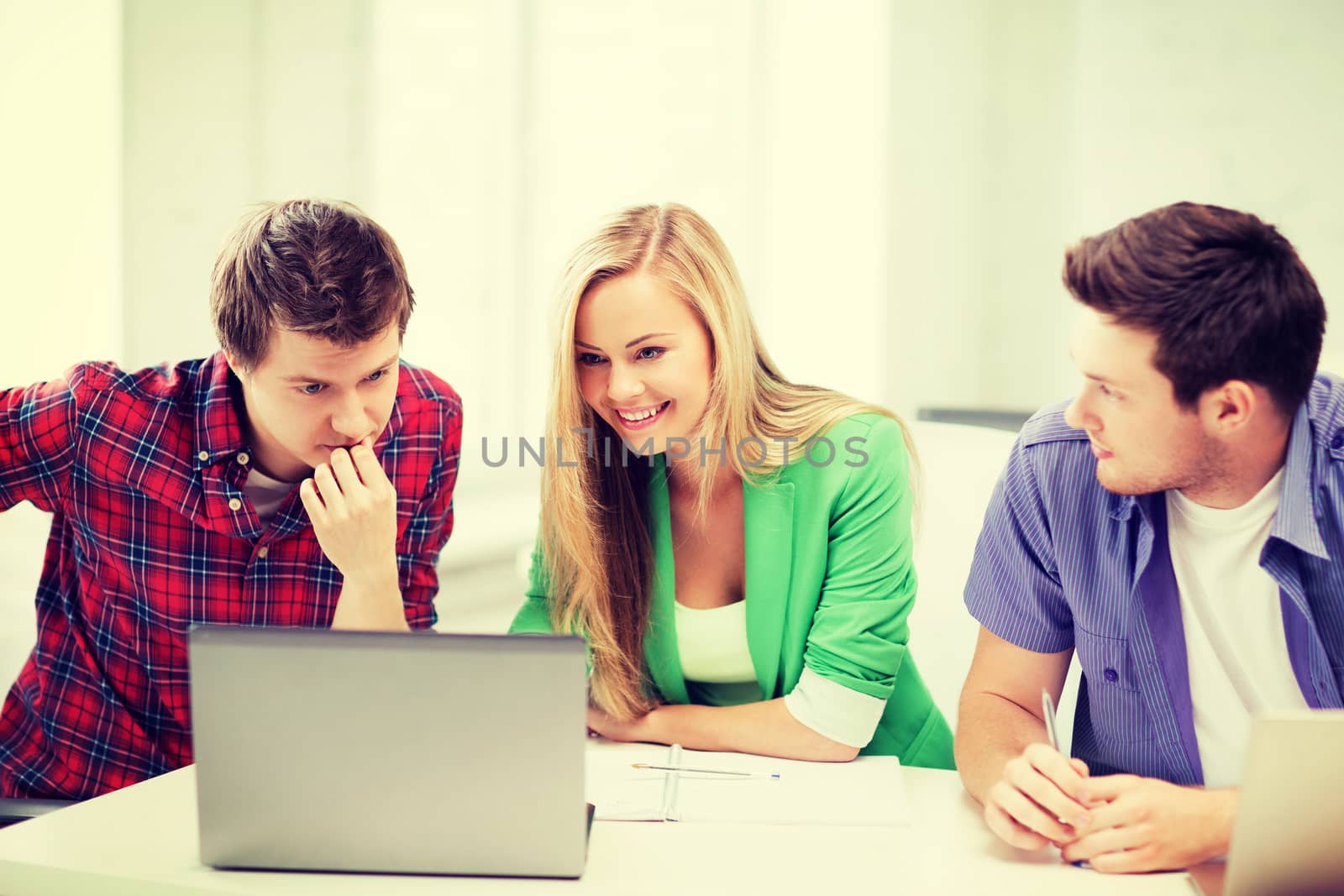 smiling students looking at laptop at school by dolgachov