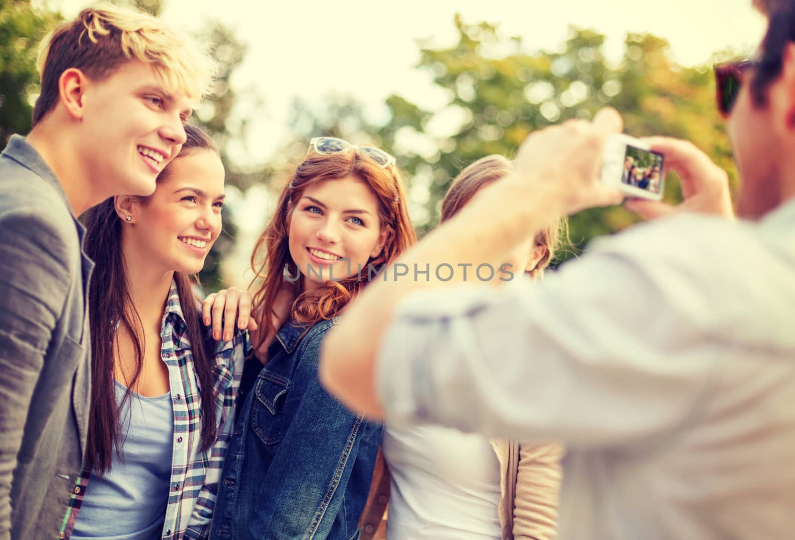 summer holidays, electronics and teenage concept - group of smiling teenagers taking photo with digital camera outside