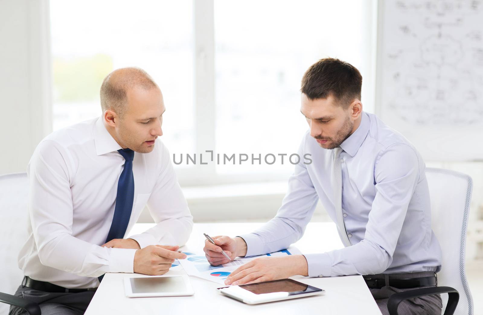 business, technology and office concept - two serious businessmen with tablet pc computers and files in office