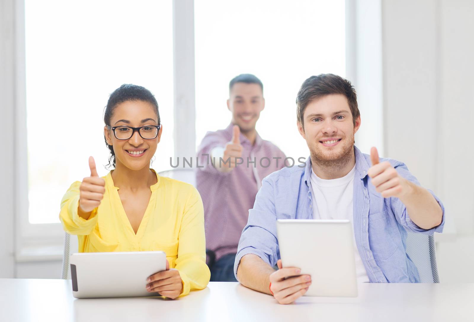 business, office and startup concept - creative smiling team with tablet pc computers at office showing thumbs up