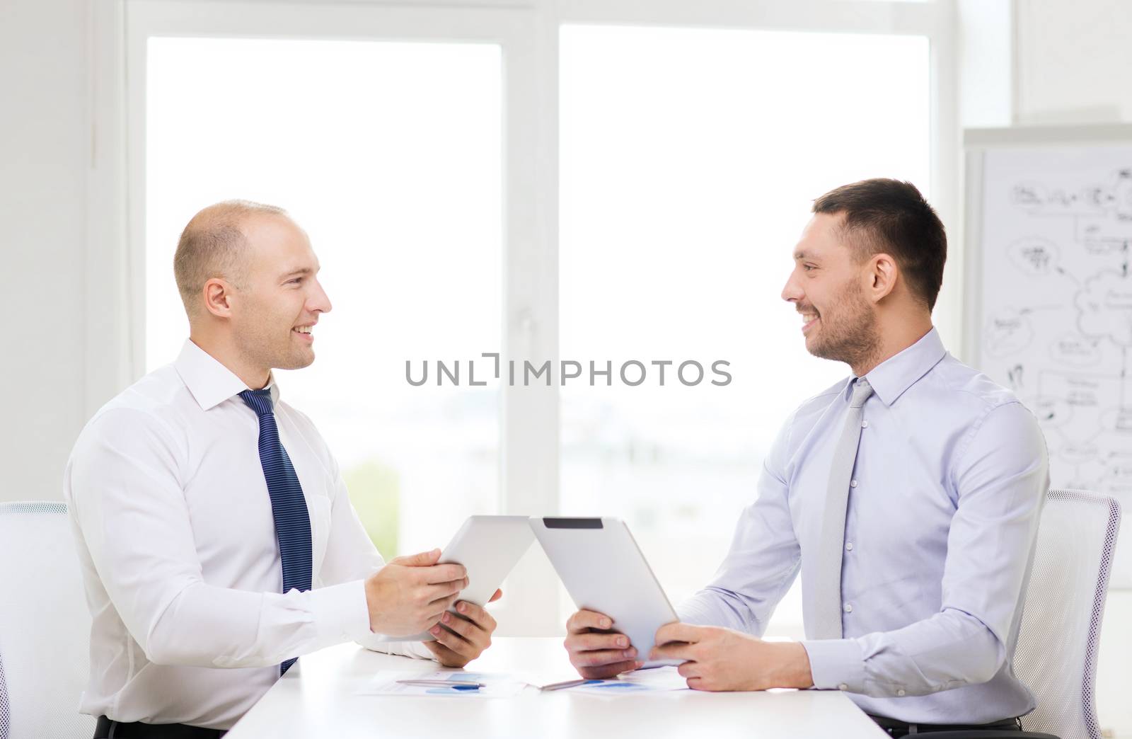 business, technology and office concept - two smiling businessmen with tablet pc computers and files in office