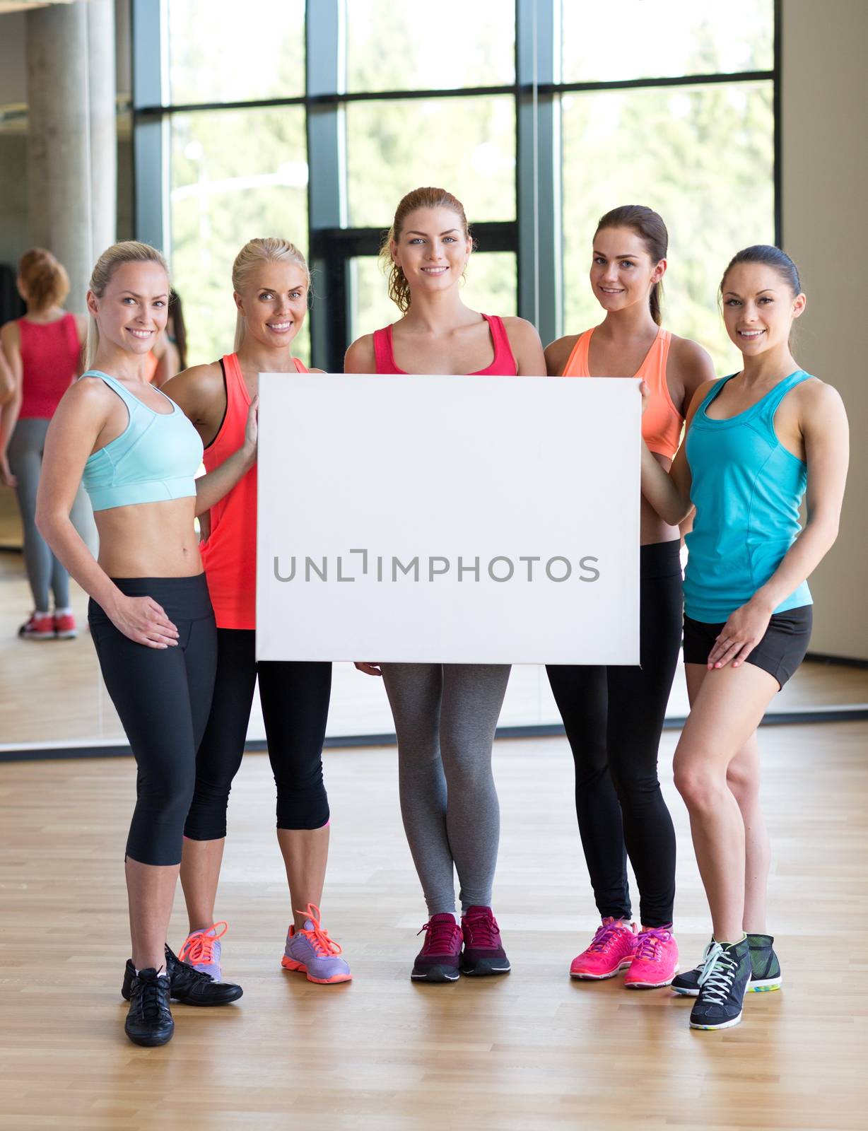 fitness, sport, training, gym and lifestyle concept - group of women witn white blank billboard in gym