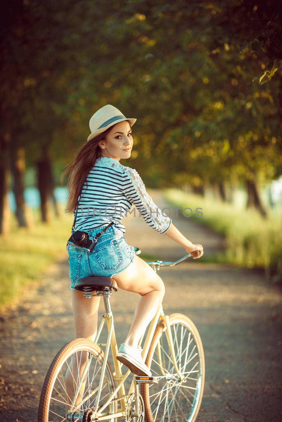 Lovely young woman in a hat riding a bicycle outdoors. Active pe by vlad_star