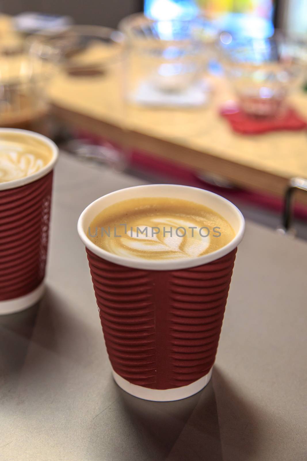 Side view of two latte art coffees with heart figure on, in take away paper glass in a cafe.