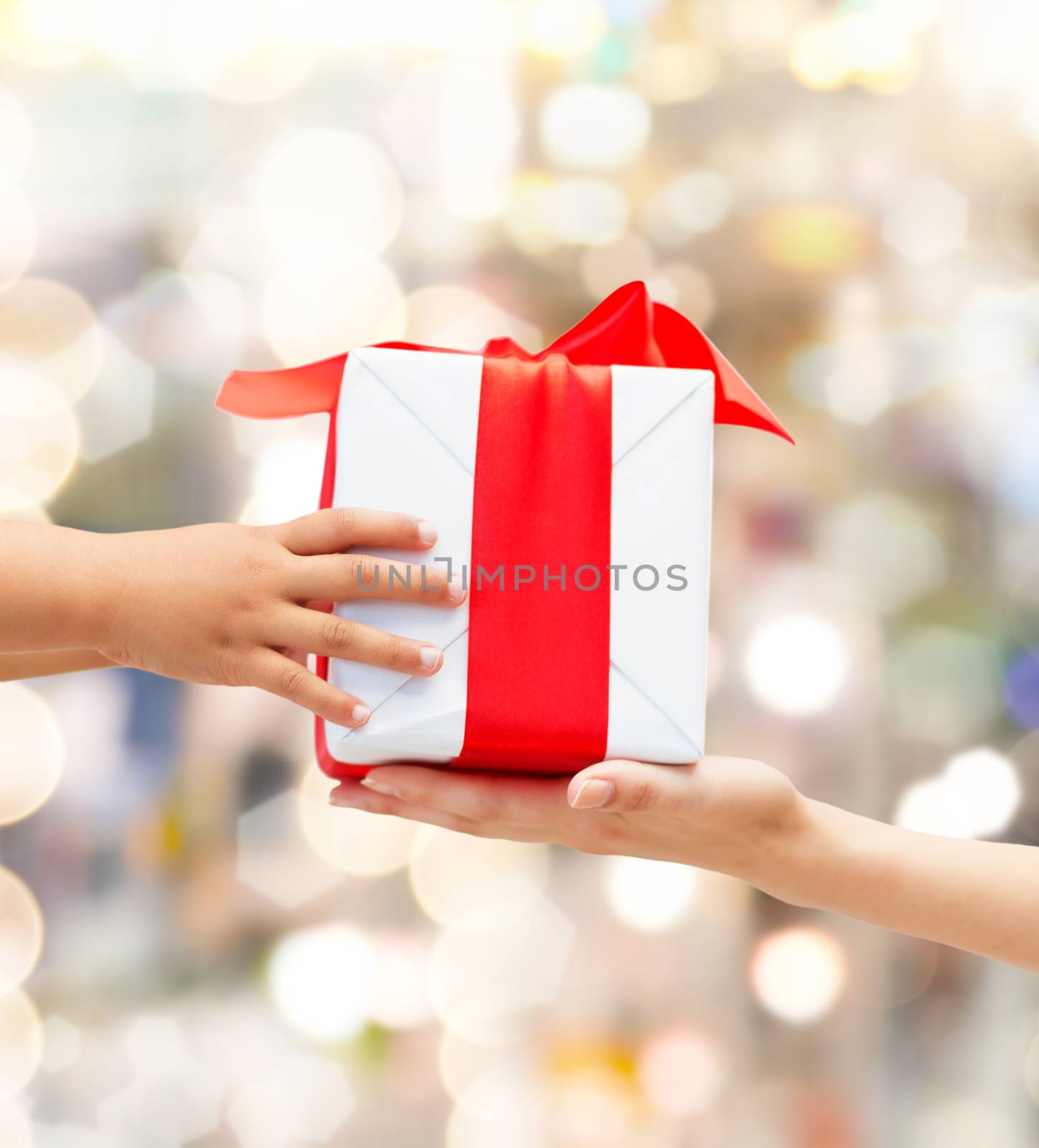 holidays, present, christmas, childhood and happiness concept - close up of child and mother hands with gift box over lights background