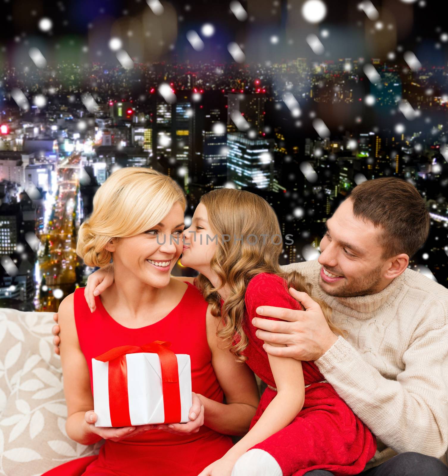 christmas, holidays, family and people concept - happy mother, father and little girl with gift box kissing over snowy night city background