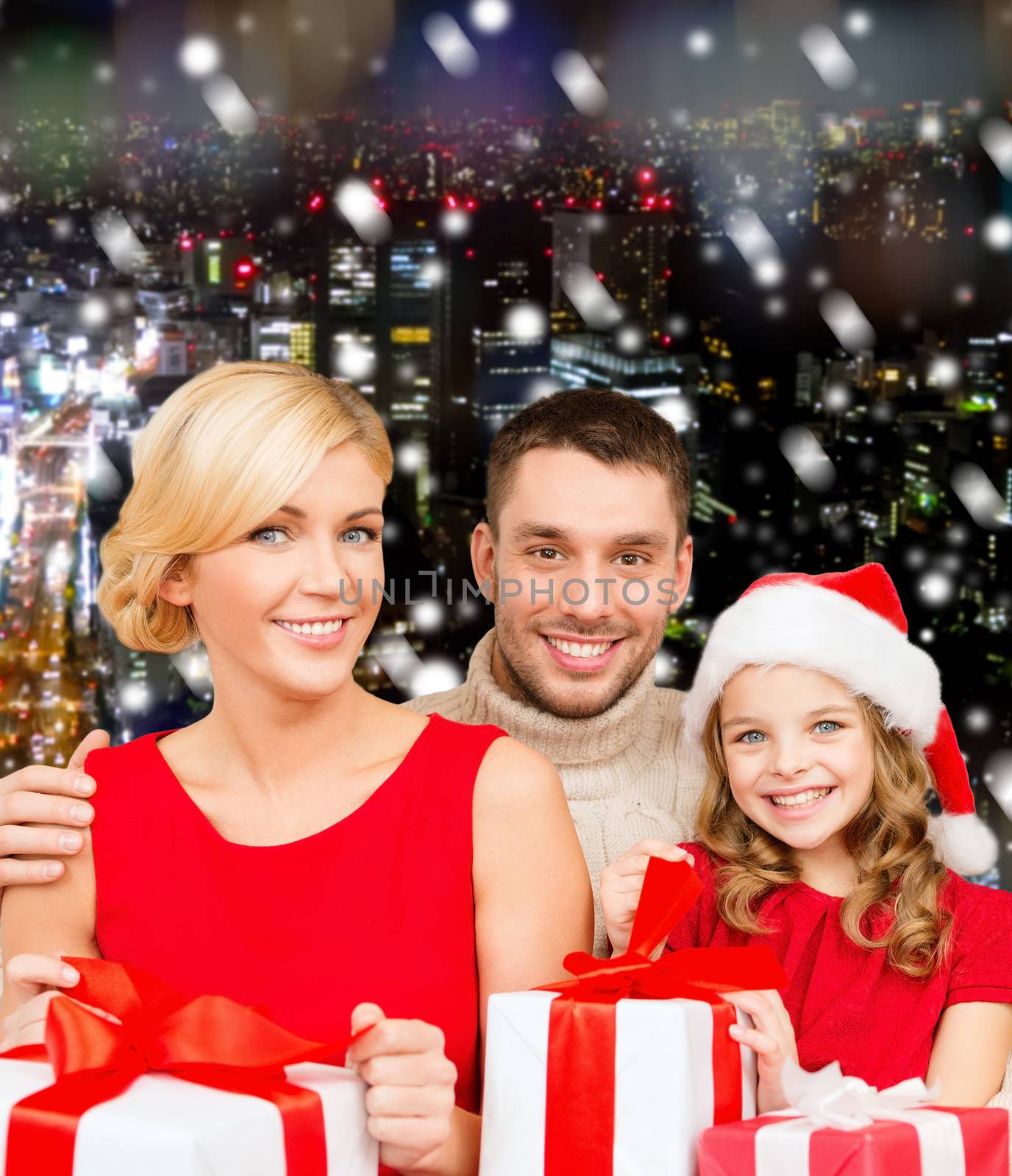 christmas, holidays, family and people concept - happy mother, father and little girl in santa helper hat with gift boxes over snowy night city background