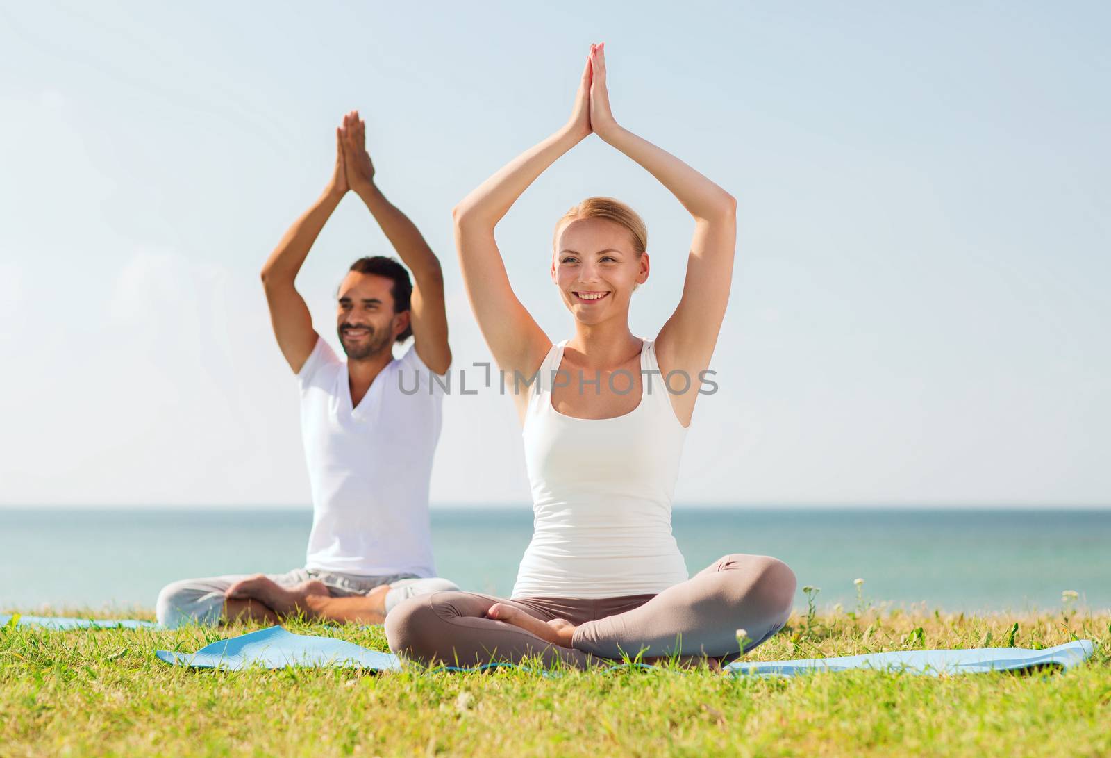 smiling couple making yoga exercises outdoors by dolgachov