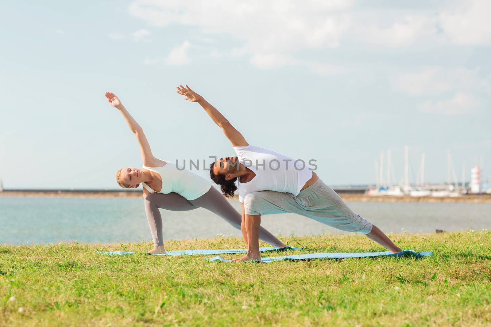 smiling couple making yoga exercises outdoors by dolgachov
