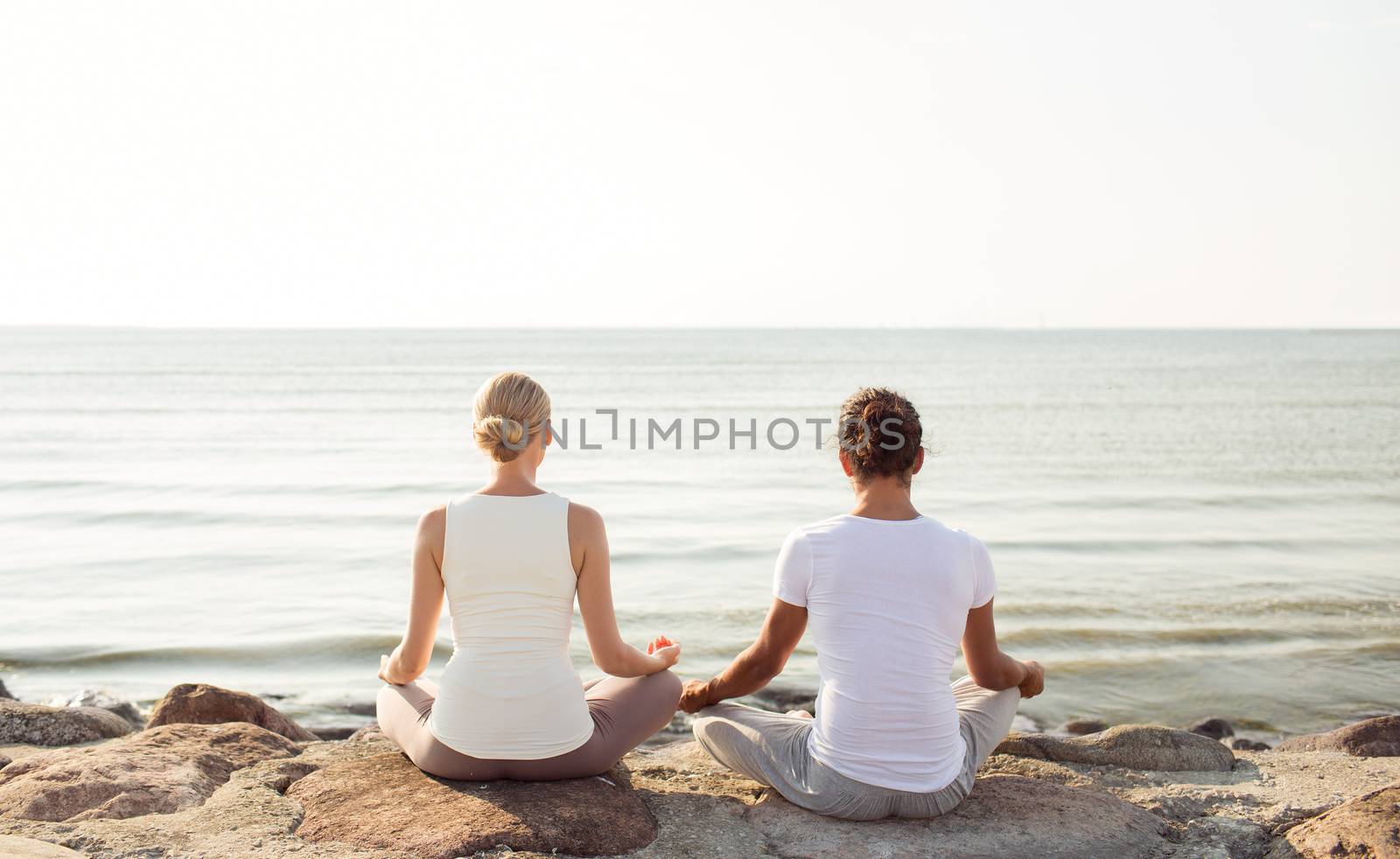 fitness, sport, people and lifestyle concept - couple making yoga exercises sitting on pier outdoors from back