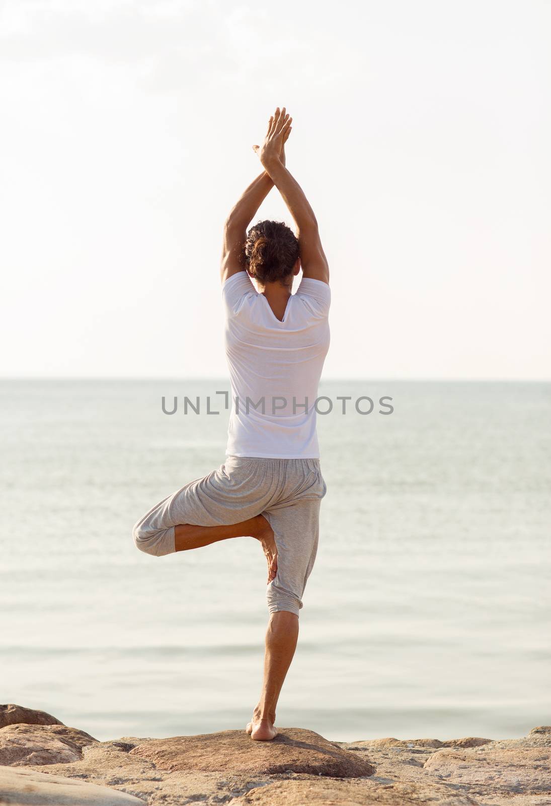 young man making yoga exercises outdoors by dolgachov