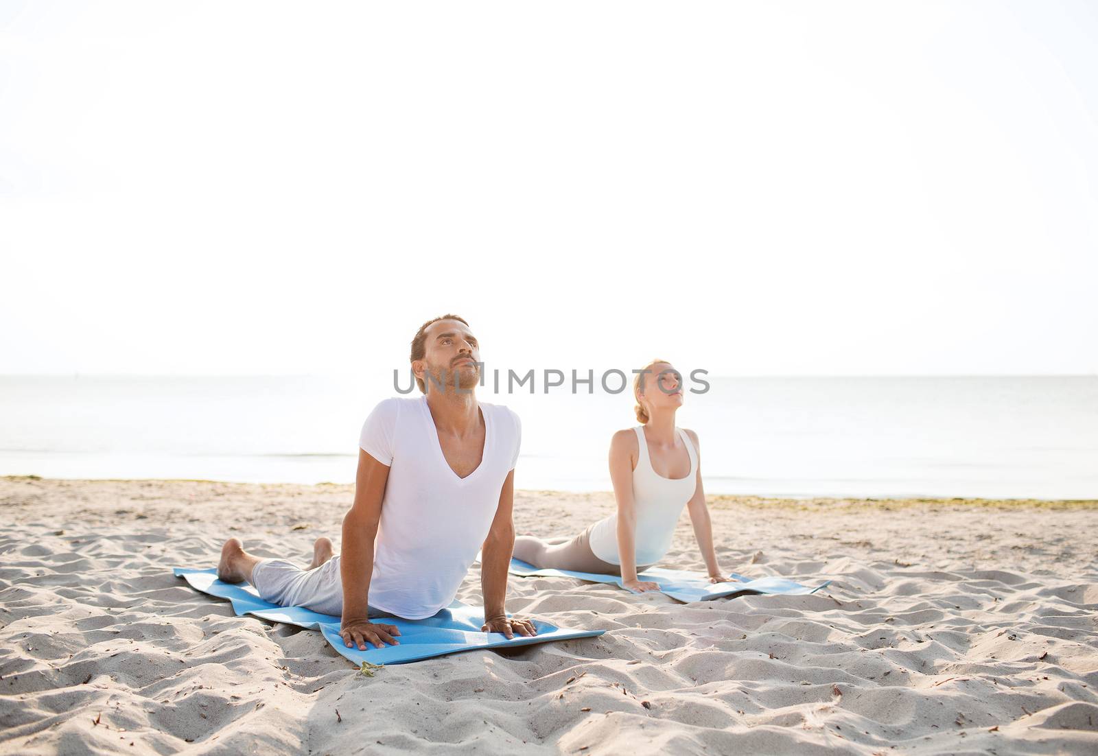 fitness, sport, friendship and lifestyle concept - couple making yoga exercises lying on mats outdoors