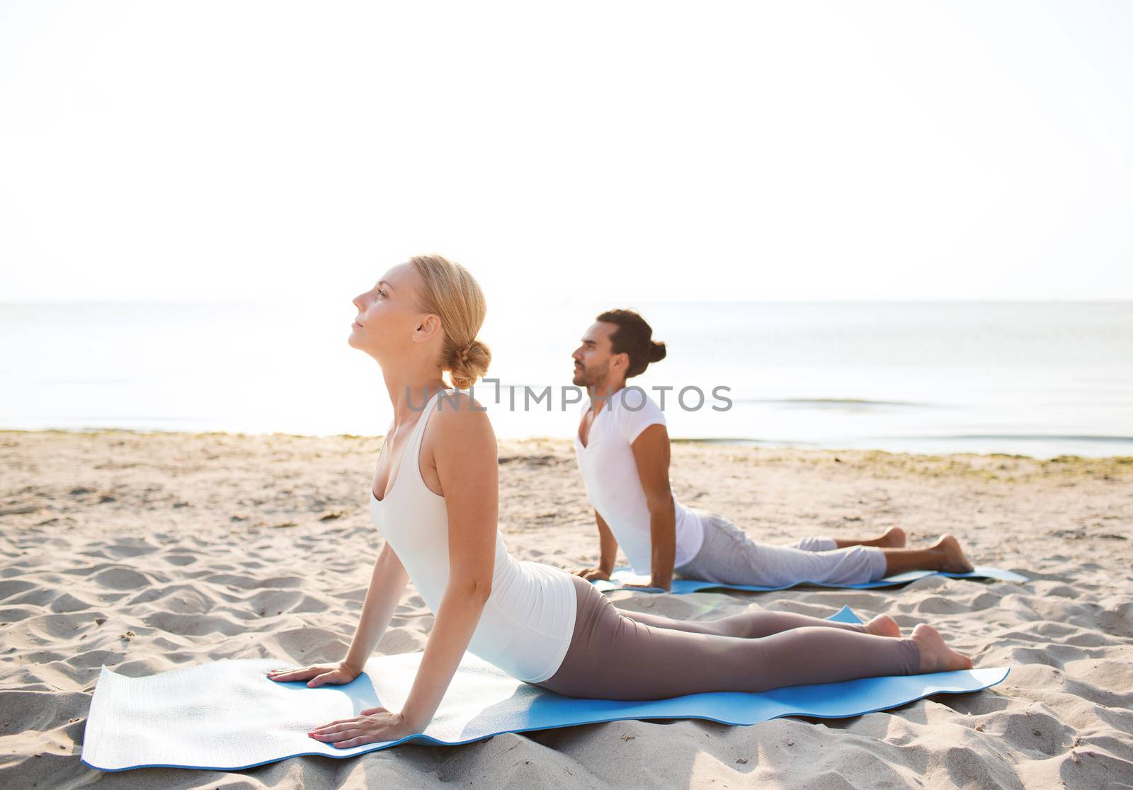 fitness, sport, friendship and lifestyle concept - couple making yoga exercises lying on mats outdoors