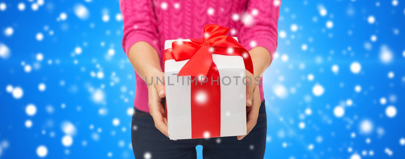 christmas, holidays and people concept - close up of woman in pink sweater holding gift box over blue snowy background