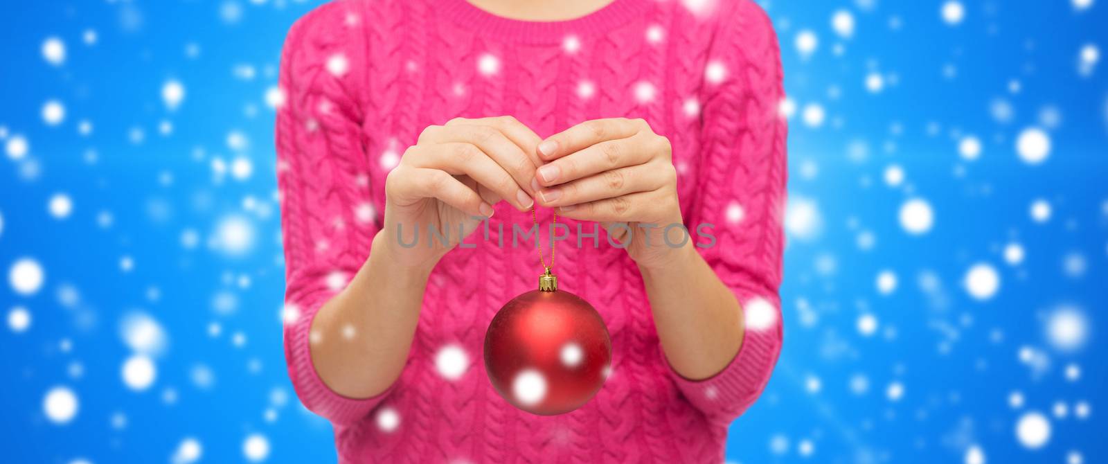 christmas, decoration, holidays and people concept - close up of woman in pink sweater holding christmas ball blue snowy background