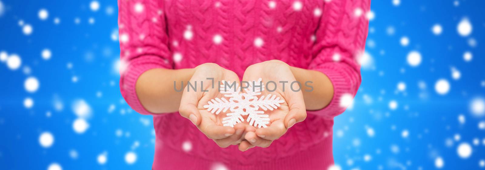 christmas, holidays and people concept - close up of woman in pink sweater holding snowflake blue snowy background