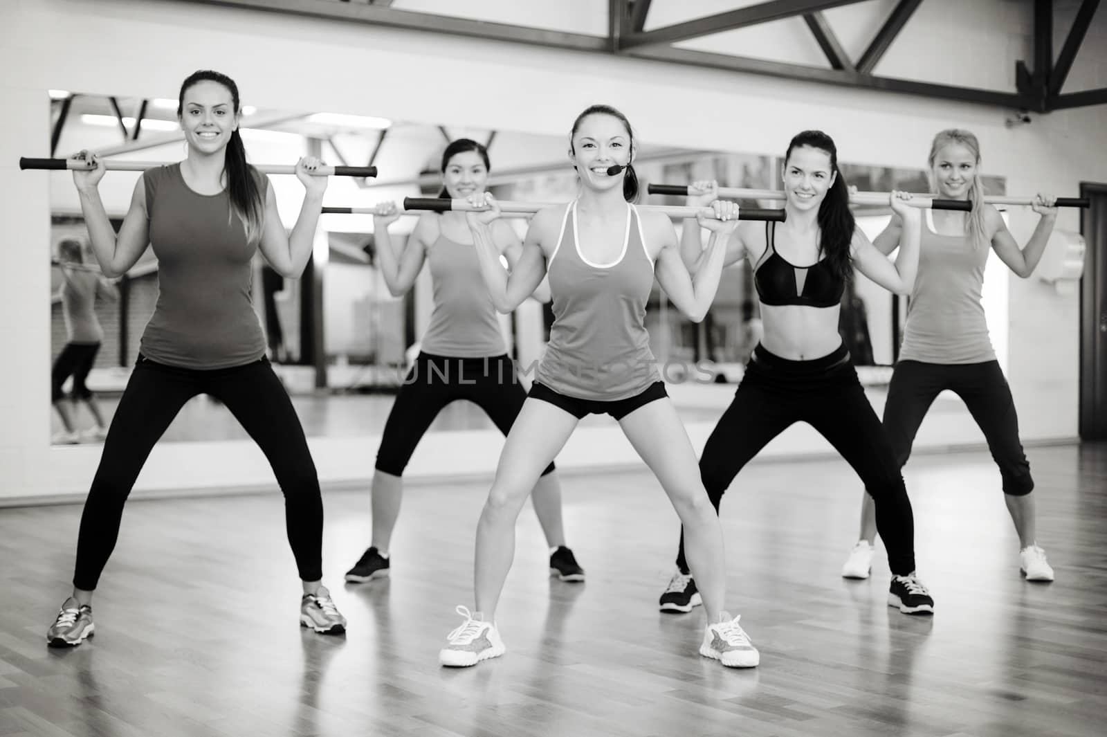 fitness, sport, training, gym and lifestyle concept - smiling trainer in front of the group of people working out with barbells in the gym
