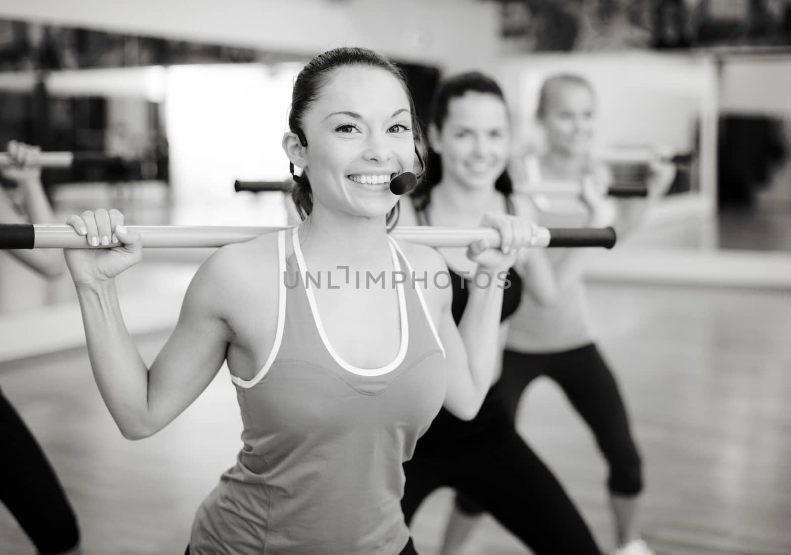 fitness, sport, training, gym and lifestyle concept - smiling trainer in front of the group of people working out with barbells in the gym