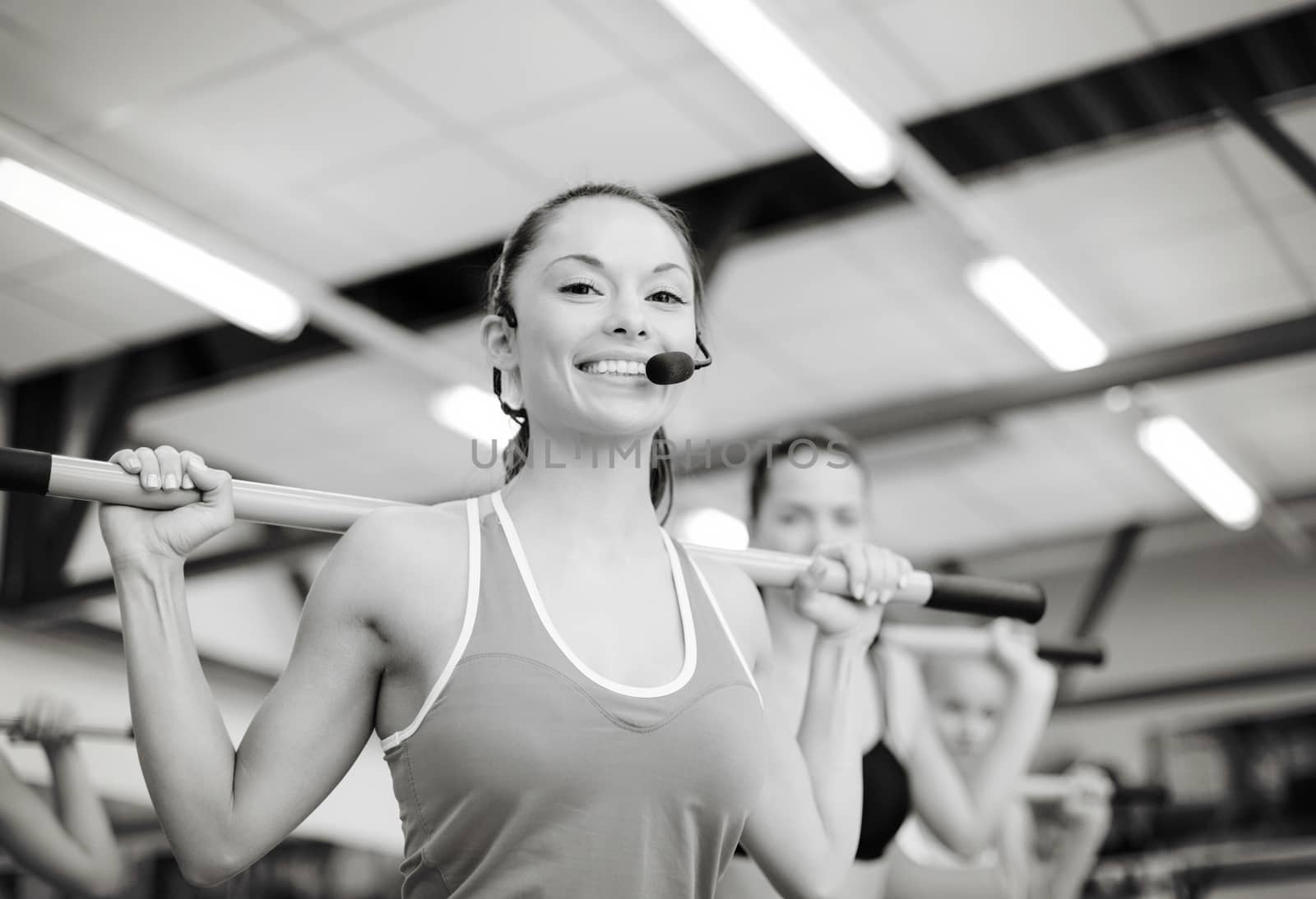 fitness, sport, training, gym and lifestyle concept - smiling trainer in front of the group of people working out with barbells in the gym