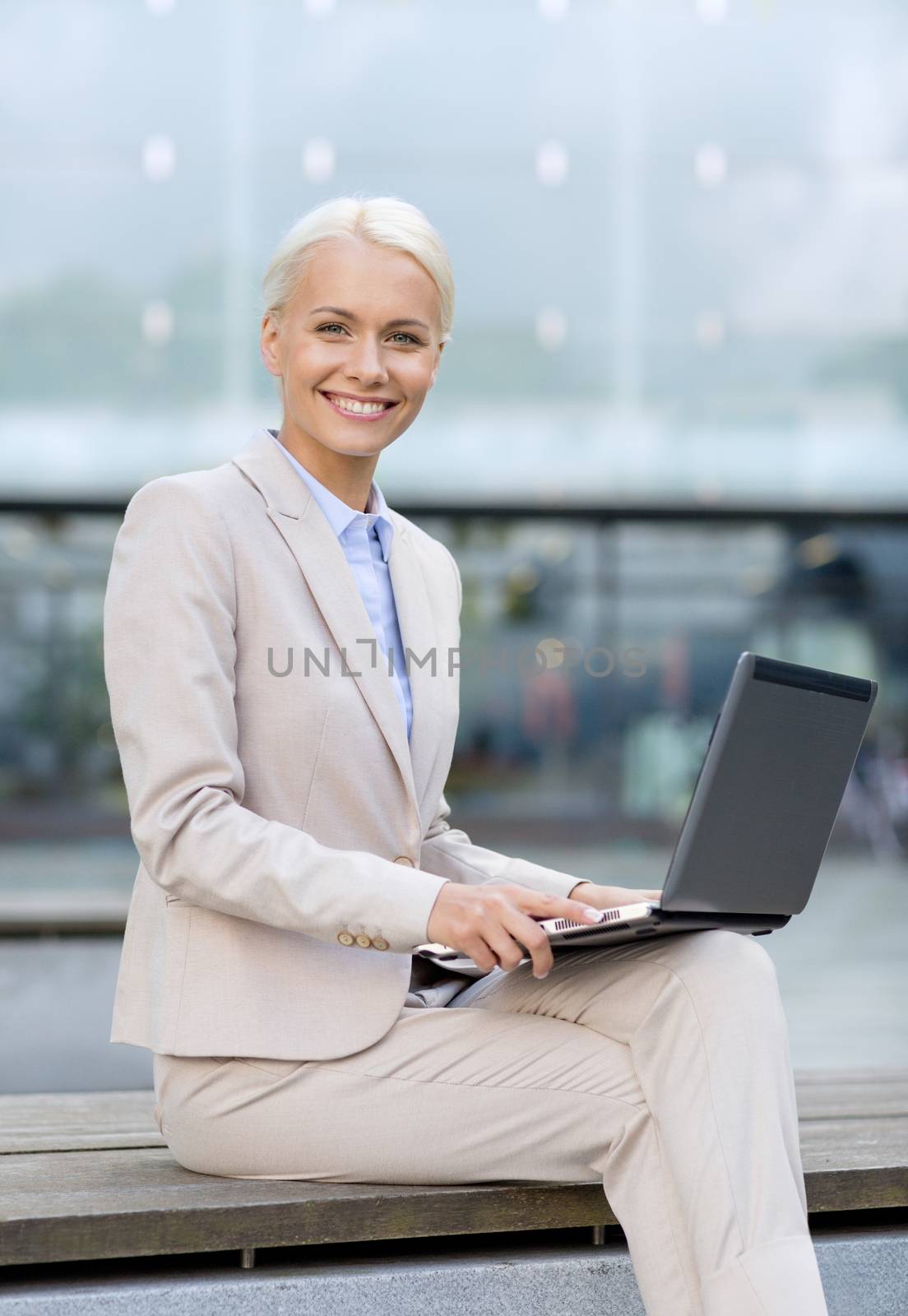 smiling businesswoman working with laptop outdoors by dolgachov