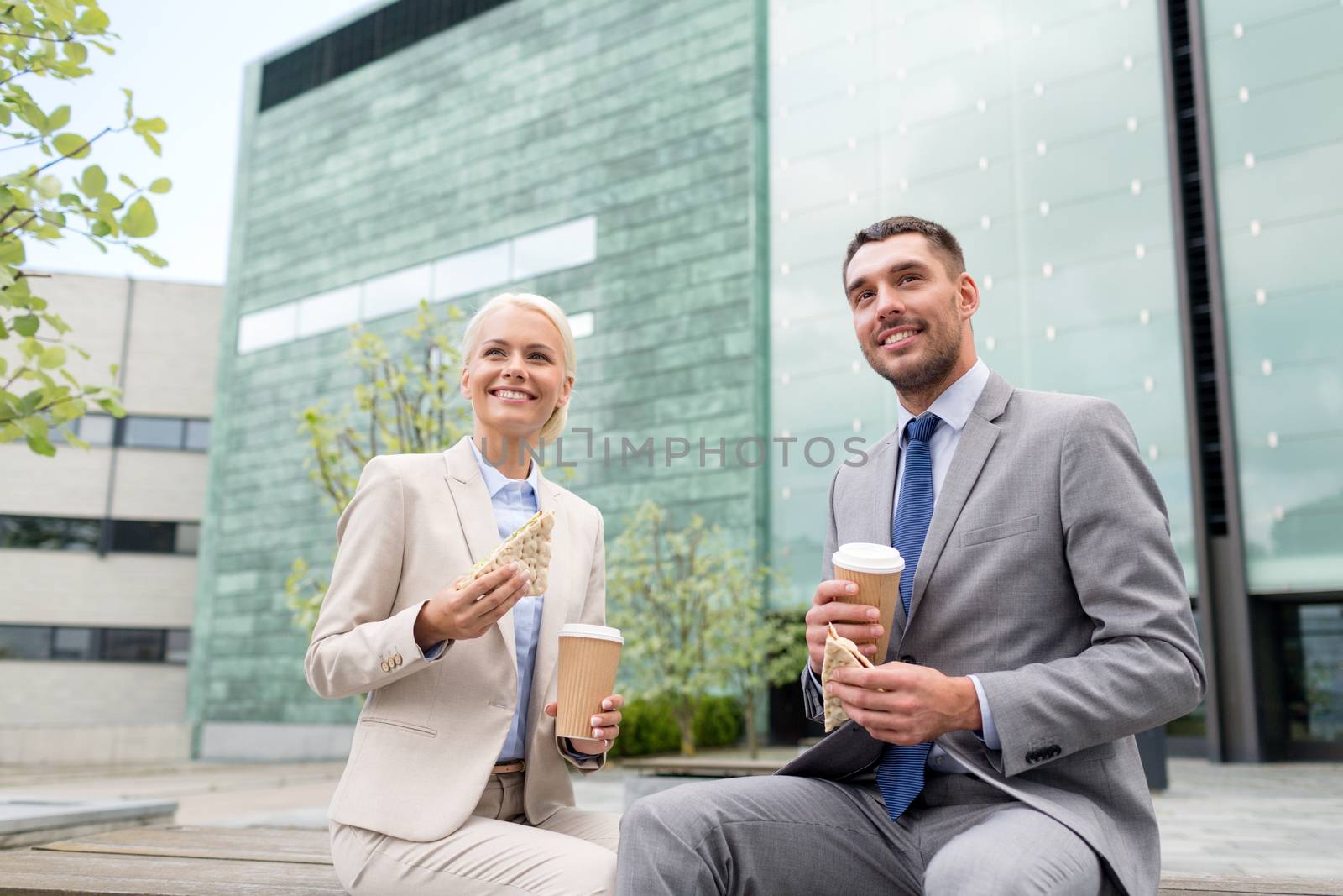 business, partnership, food, drinks and people concept - smiling businessmen with paper cups standing over office building