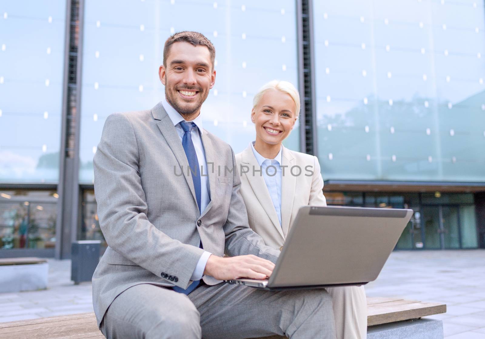 smiling businesspeople with laptop outdoors by dolgachov
