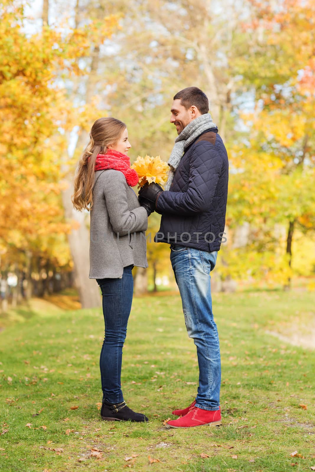 smiling couple with bunch of leaves in autumn park by dolgachov