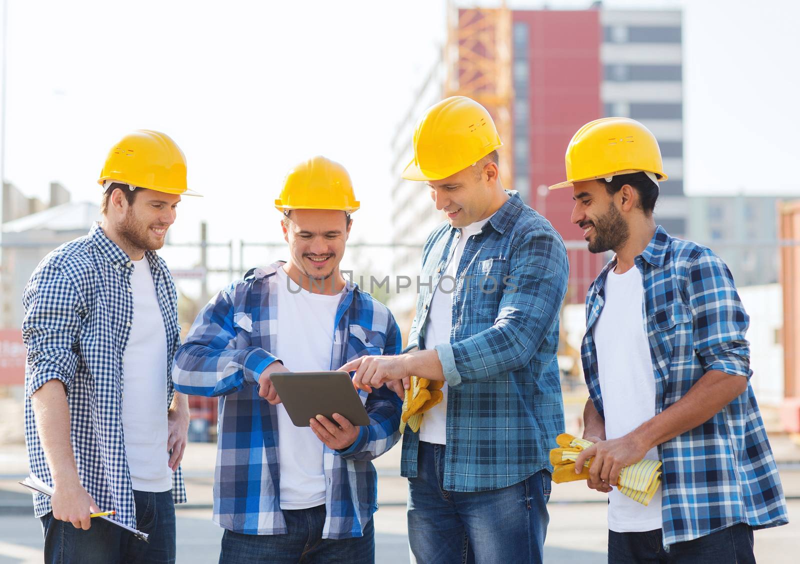 business, building, teamwork, technology and people concept - group of smiling builders in hardhats with tablet pc computer and clipboard outdoors