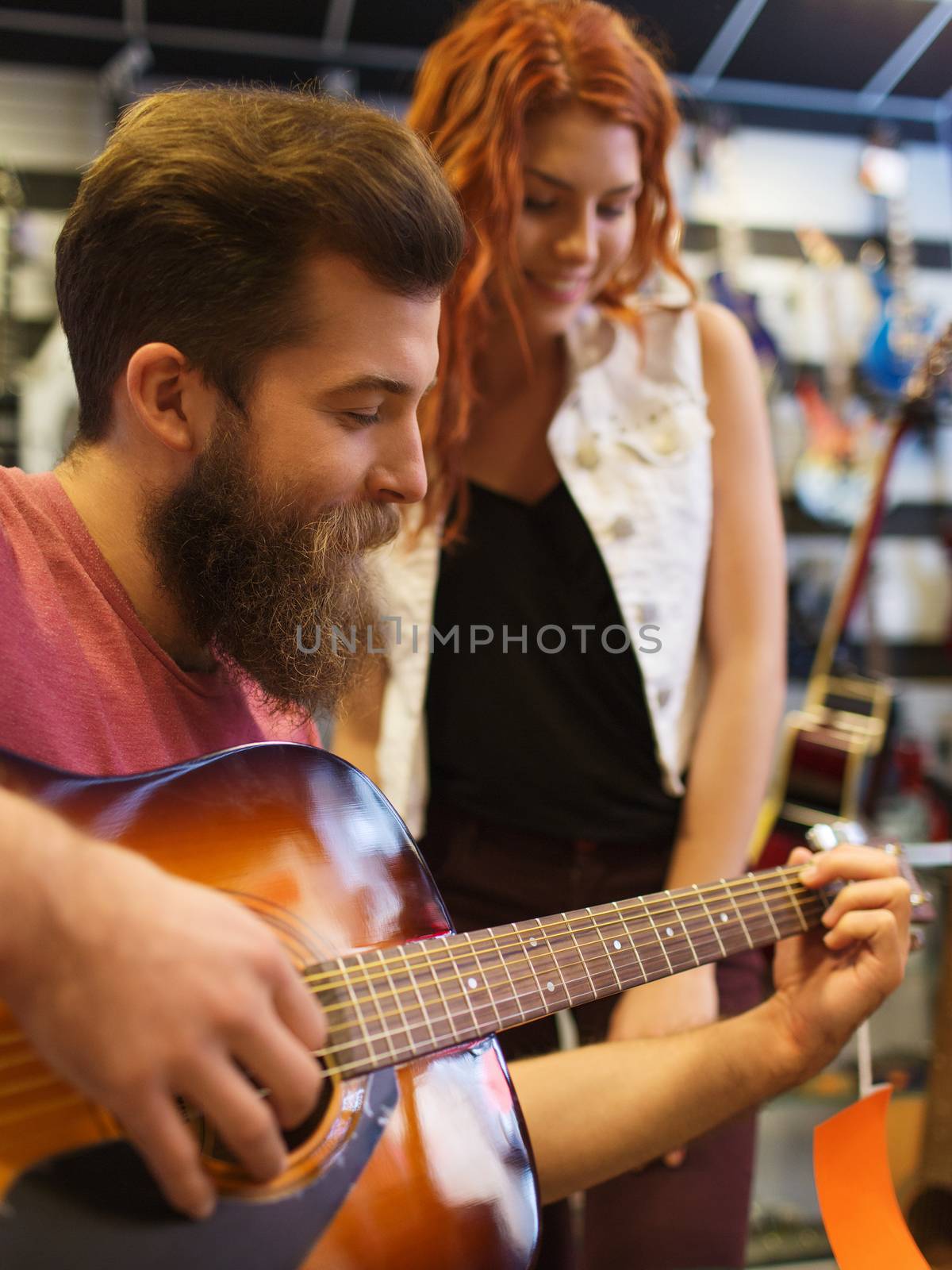 music, sale, people, musical instruments and entertainment concept - happy couple of musicians with guitar at music store