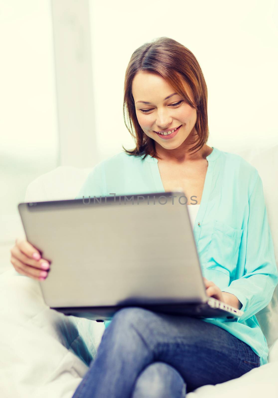 home, technology and internet concept - smiling woman sitting on the couch with laptop computer at home