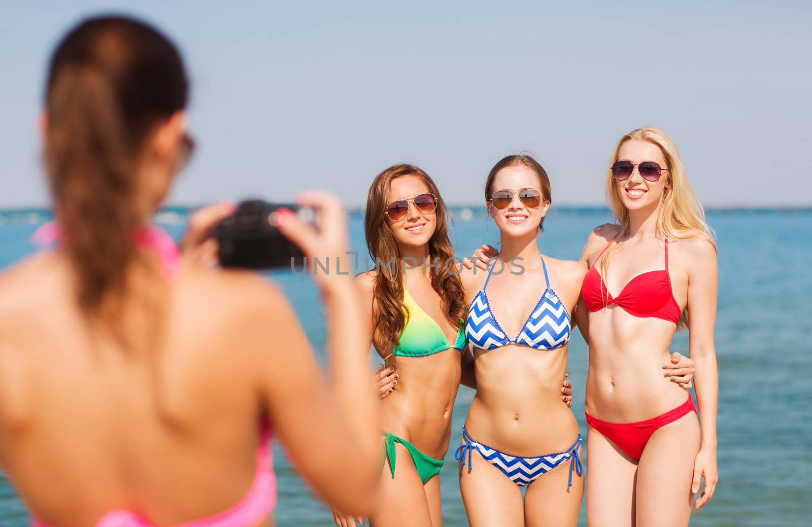 group of smiling women photographing on beach by dolgachov