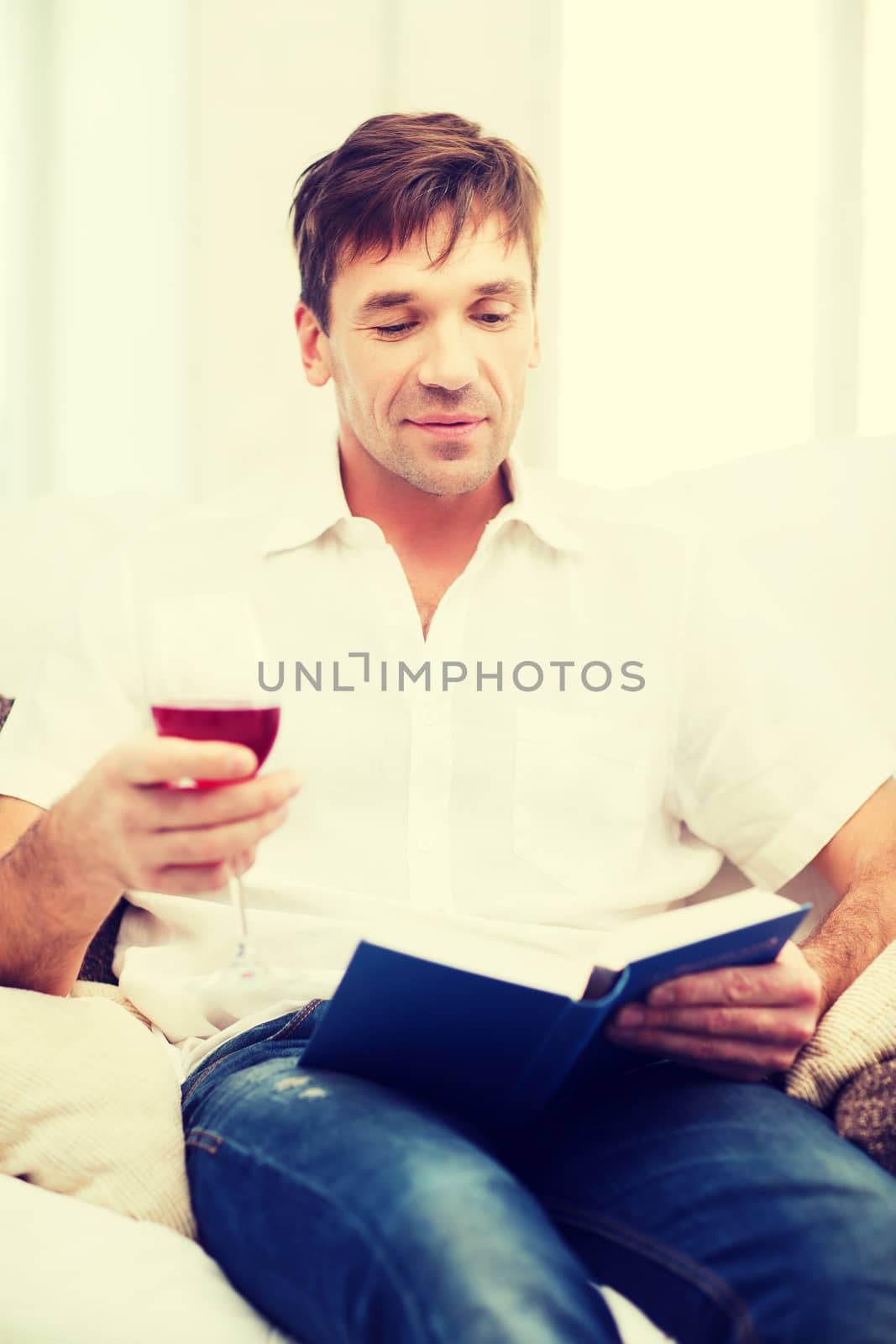 happy man with book and glass of rose wine at home by dolgachov