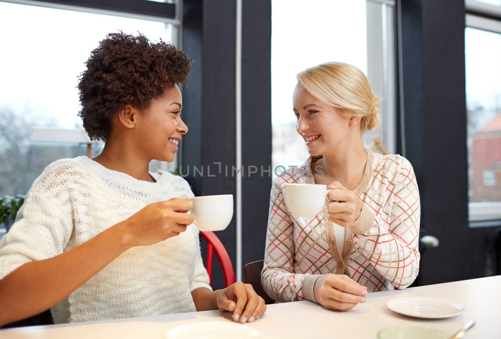 happy young women drinking tea or coffee at cafe by dolgachov