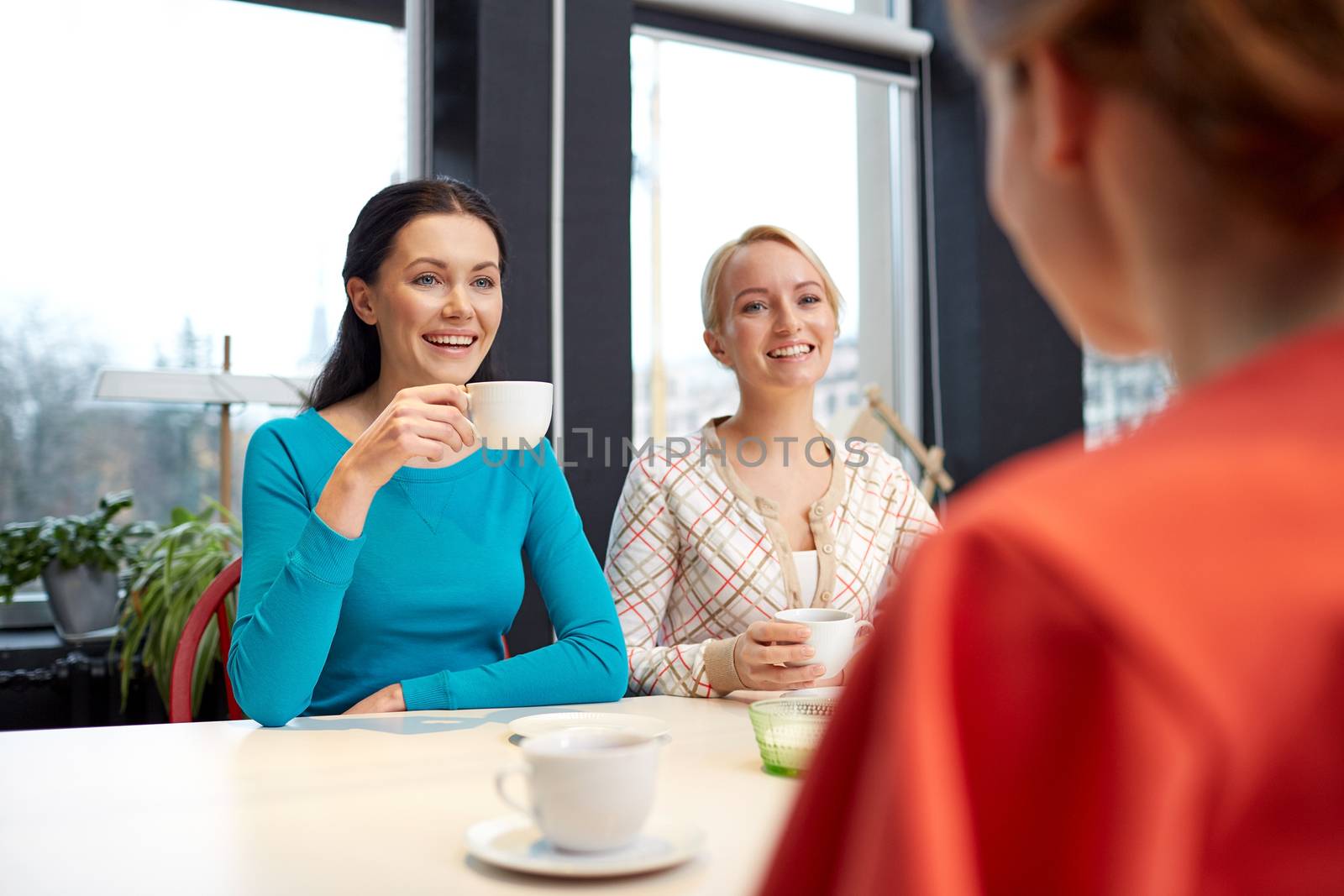 people, leisure, friendship and communication concept - happy young women meeting and drinking tea or coffee at cafe