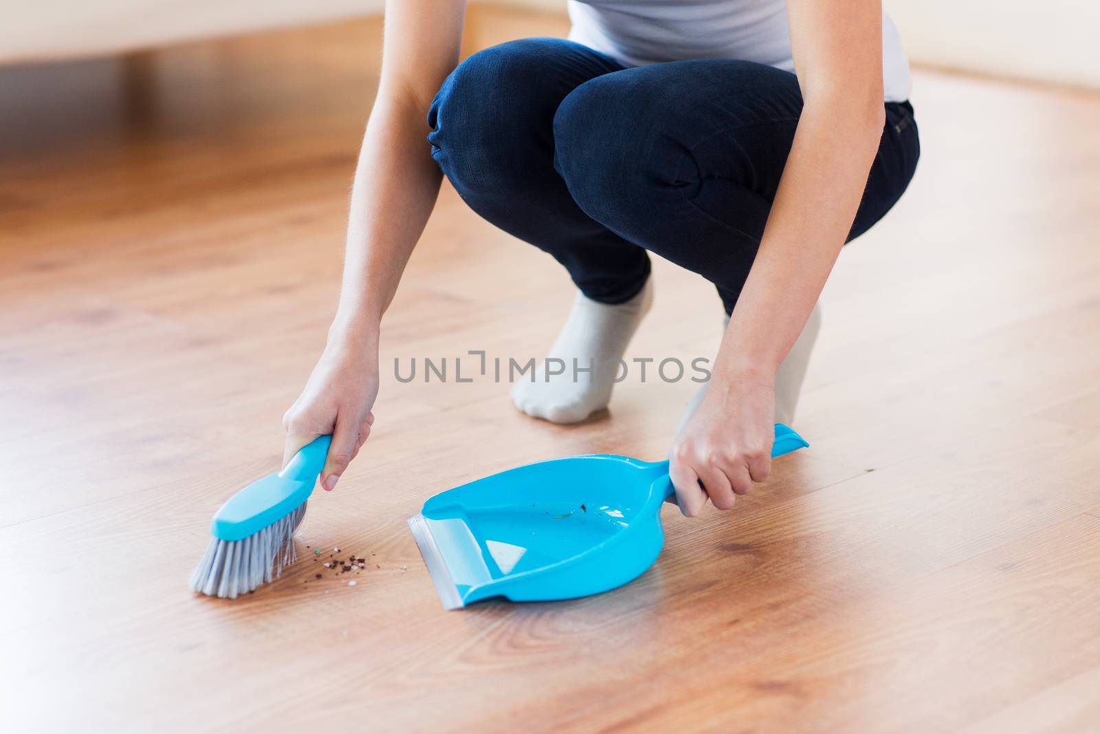 people, housework, cleaning and housekeeping concept - close up of woman with brush and dustpan sweeping floor at home