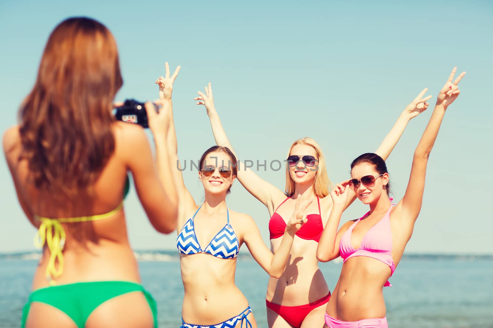 group of smiling women photographing on beach by dolgachov